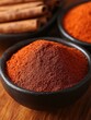 © punniix - A close-up of a mound of vibrant red spice in a bowl, surrounded by cinnamon sticks, showcasing rich colors and textures.