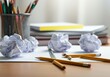 © Alexandra - Writer experiencing creative block sits at desk with crumpled paper, broken pencils and notebooks, struggling with ideas and feeling frustrated with writing process