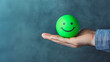 © Concept Island - Customer service evaluation, customer satisfaction good level and satisfaction survey concept. Man hand holds a green smiling ball, isolated in a blue background