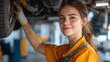 © Pinklife - A smiling female mechanic in a yellow uniform works on a vehicle's undercarriage, emphasizing a positive attitude and dedication to her craft.