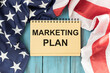 © Pawel - Notebook with text marketing plan on table with American flag