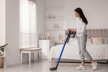 Young woman cleaning floor with cordless vacuum cleaner in bedroom