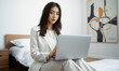 © RooftopStudioBangkok - business woman in white suit working on laptop in modern bedroom, exuding professionalism and focus. stylish decor enhances atmosphere