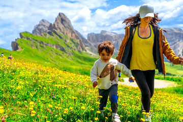 Mother and son running through wildflower meadow in seceda, dolomites