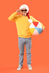 Sticker - Happy young man in Santa hat with inflatable ball on orange background