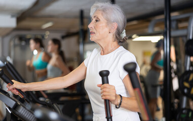 Canvas Print - Mature sportswoman training at elliptical machine in modern gym