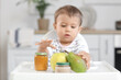 © Pixel-Shot - Cute little baby with jars of tasty food and fruits sitting on chair in kitchen at home