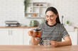 © Pixel-Shot - Beautiful young happy woman pouring hot tea from transparent kettle into cup in kitchen