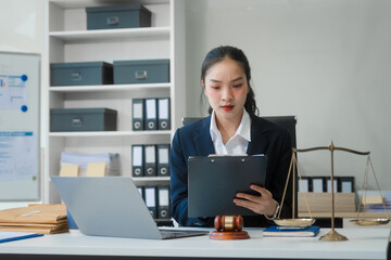 Wall Mural - A young Asian woman in a suit works at her desk, reviewing legal documents. lawyer advice on contracts, finance, agreements, demonstrating professionalism and authority in business setting.