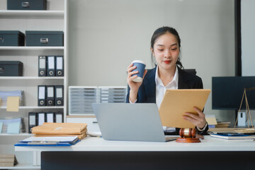 Wall Mural - A young Asian woman in a suit works at her desk, reviewing legal documents. lawyer advice on contracts, finance, agreements, demonstrating professionalism and authority in business setting.