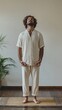 © Maria Mikhaylichenko - Mindful meditation practice in comfortable linen outfit against neutral wall background, standing barefoot on bamboo mat with decorative palm plant, embodying zen lifestyle.