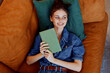© SHOTPRIME STUDIO - Woman resting and reading a green book on couch in denim shirt in cozy home setting