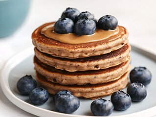 Wall Mural - Delicious pancakes stacked high, topped with creamy nut butter and fresh blueberries, served on a white plate.