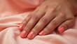 © Vladimir - Stylish hand with soft coral nails resting on smooth pink satin fabric