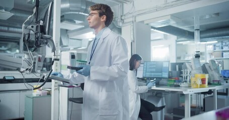 Aufkleber - Portrait of a Young Male Scientist Holding a Set of Test Tubes and Using a Computer while Standing in a Modern Medical Research Laboratory. Asian Female Colleague Working in the Background
