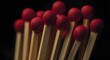 © DesignHubpro - A close up of a set of wooden matches arranged on an isolated dark background. The match heads are red in color and the wooden sticks have a natural texture. The sticks are ready to use.