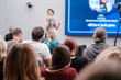 © Anton Gvozdikov - Diverse group sitting in audience listening to a speaker at professional conference or seminar. Blurred presenter and screen in background.