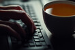 © Seema Designs - close-up of a hand typing on a keyboard with a cup of tea