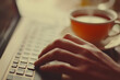 © Seema Designs - close-up of a hand typing on a keyboard with a cup of tea
