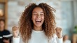 © svastix - A woman with curly hair in a white sweater is joyfully celebrating, displaying a wide smile and raised fists, embodying excitement and happiness.