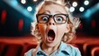 © svastix - A young child with wide eyes and an open mouth sits in a theater, displaying an expression of amazement or shock while lights glow in the background.