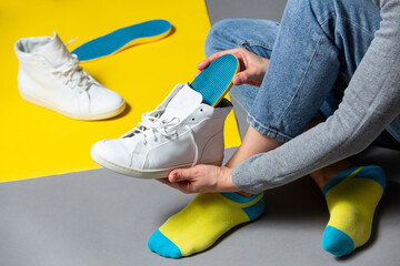 Close up of female hands putting orthopedic insoles inside white sneakers .