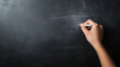 © Bonsales - Teacher's hand writing on blackboard with white chalk, creating dust particles in dim classroom