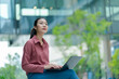 © Yingyaipumi - Business people thinking with laptop computer.Businesswomen outdoor working at green city background.Asia Business female sitting on big city urban street outside.City Streets With People concept