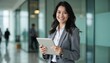© schiers_images - A confident businesswoman in a modern office setting, smiling while holding a digital tablet. The scene conveys professionalism, success, and technology in the workplace environment.