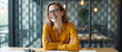 © schiers_images - A cheerful businesswoman sitting at her desk, exuding confidence and positivity. Her bright yellow shirt adds a vibrant touch to her professional demeanor in the modern office setting.