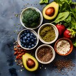 © shustrilka - assortment of fresh, colorful fruits and vegetables including avocados, blueberries, greens, camera bloom, fresh fruit color scheme, top view on grey background, surrounded by bowls with grains