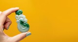 Hand holding intricate green jade pendant on yellow background Female with painted nails