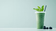 © INT888 - refreshing green smoothie in to go cup with straw, garnished with fresh basil leaves, sits next to ripe blackberries on light background