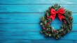 © Kultivad - Green Christmas wreath adorned with red bow and berries on vibrant blue wooden background for festive holiday decoration concept