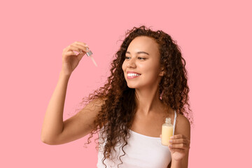 Canvas Print - Beautiful young African-American woman with bottle of face serum on pink background