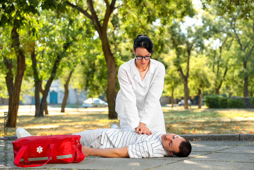Female doctor doing CPR on unconscious man having heart attack in park