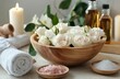 © jahanarabegum7973 - A wooden bowl with white flowers inside, surrounded by spa products like candles and salt pebbles on the table. A towel is folded in front of it, while another rose petal lies next to an oil bottle