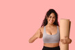 © Pixel-Shot - Sporty young African-American woman with yoga mat showing thumb-up gesture on pink background