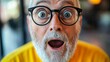 © Radomir Jovanovic - An elderly man with round glasses and a gray beard opens his mouth in surprise against a blurred indoor background, capturing an expression of amazement and wonder.