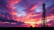 © Din Nasahrudin - Telecommunications tower at sunset, vibrant sky with purple and orange hues, silhouetted structure, technology and connectivity theme, dramatic clouds