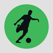 © Dima - Green and round flat icon with black silhouette of a soccer player kicking a ball. Vector on a gray background
