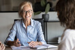 © fizkes - Smiling elderly businesswoman engaged in positive conversation with clients, laughing, while share information, engaged in negotiations, hold briefing event. Professional collaboration and mentorship