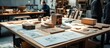 © adiba - Wooden models and blueprints on a table in a workshop with a person in the background.