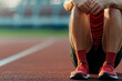 © JK_kyoto - runner sits on track, holding their knees, showing signs of discomfort and fatigue. focus is on their red shoes and athletic attire, capturing essence of sports and physical exertion