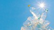 © Atthasit - Sunlight shines on a pile of plastic bottles, highlighting the environmental issue of plastic waste against a clear blue sky.