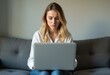 © Vibudhaart - A woman sits on a couch and uses her laptop.