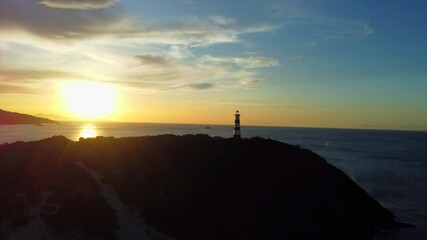 Wall Mural - A lighthouse is on a rocky shoreline with a beautiful sunset in the background