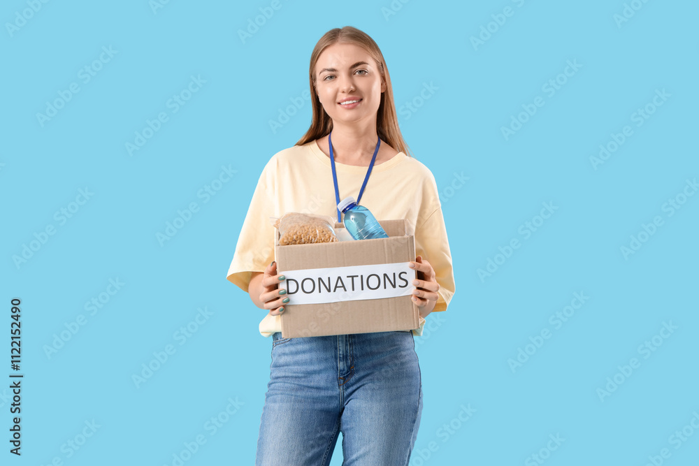 Young female volunteer with donations on blue background