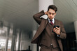© dikushin - Low-angle view of worried businessman in brown suit looking surprised and concerned while checking phone standing outdoors in urban setting. Concept of business communication and technology.