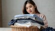 © narumiaegis - Feel softness, chore of pretty asian young woman hand holding pile clothing from table, stack folding clean clothes after washing, laundry and dry. Household working at home. Laundry of maid concept.